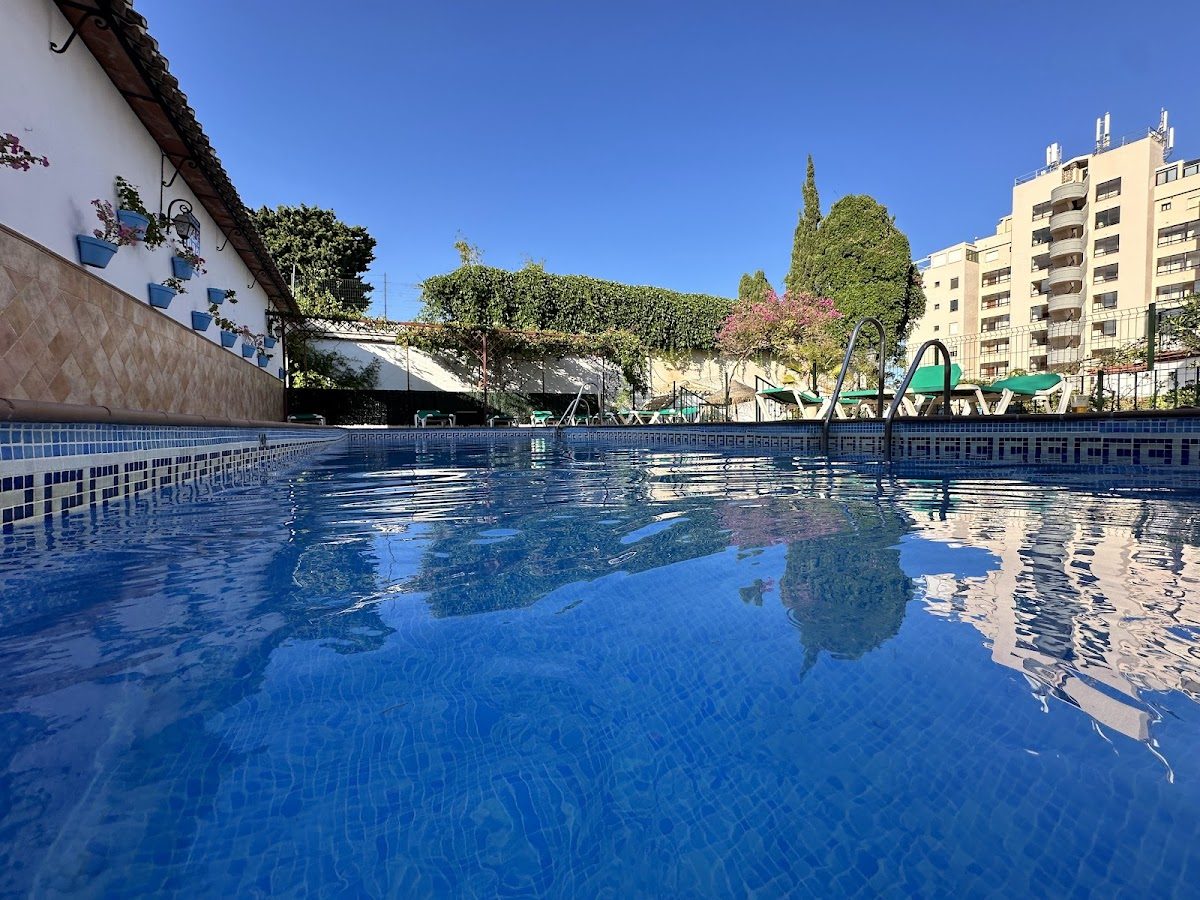 The image shows a clear swimming pool surrounded by greenery at Hotel Carmen Teresa in Torremolinos.