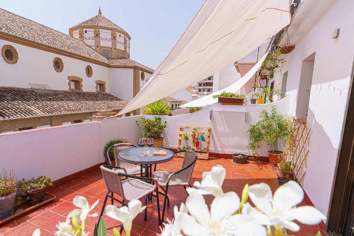 Una encantadora terraza en el Hotel Colón con mesa, sillas y plantas en macetas, con vistas a la arquitectura circundante.