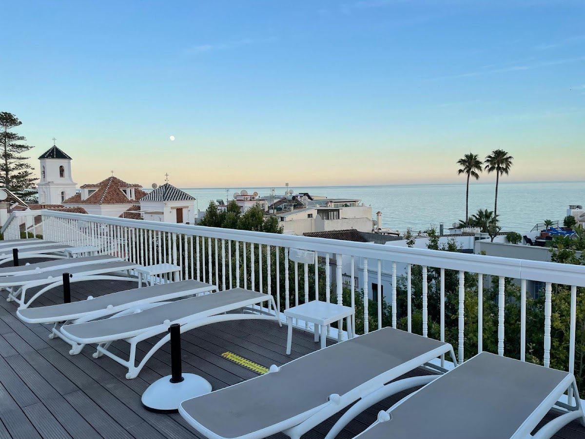 Rooftop view from Hotel Plaza Cavana featuring sun loungers, palm trees, and the sea at sunset.