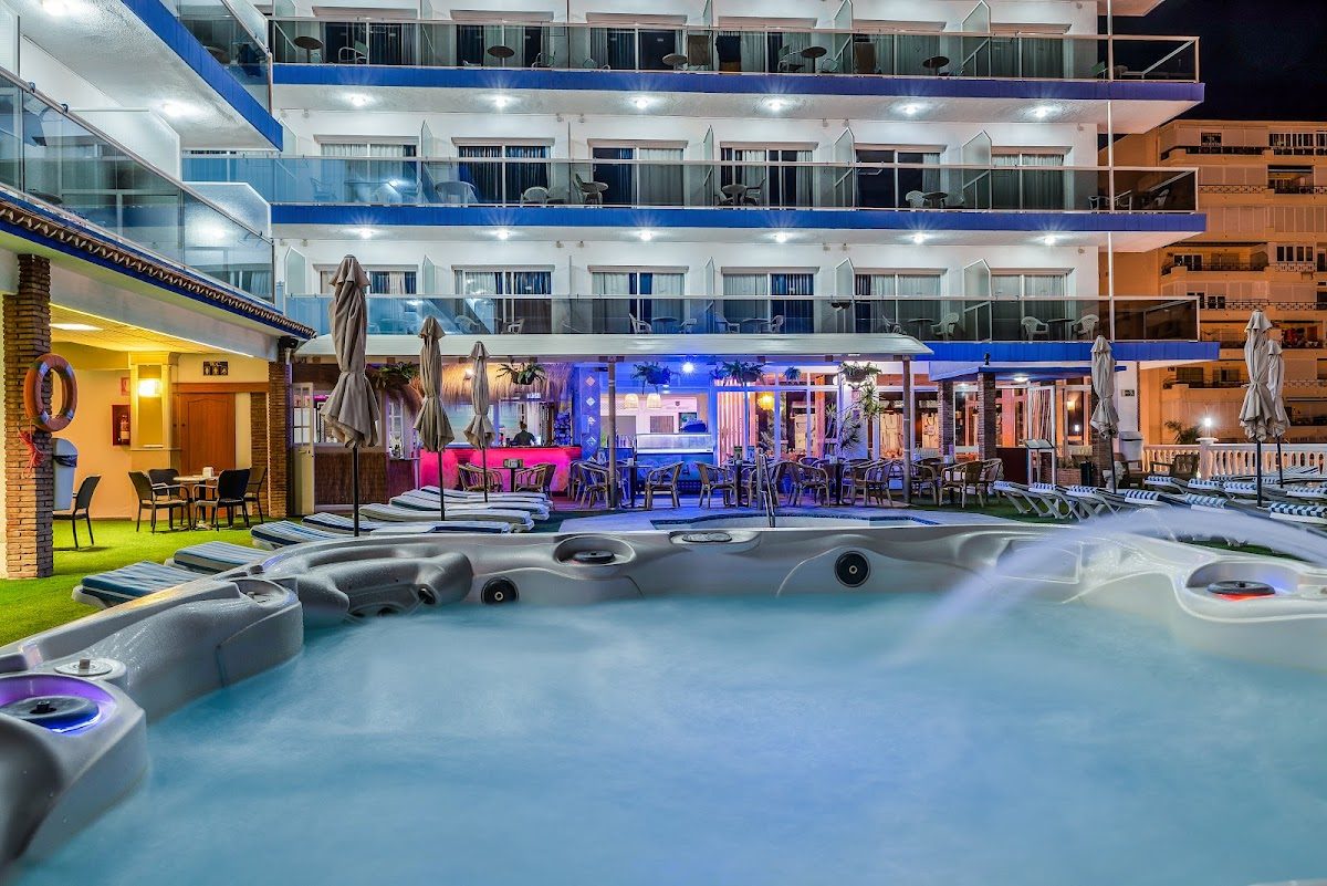 The image shows a night view of Hotel Princesa Solar's pool area with loungers and a lively atmosphere.