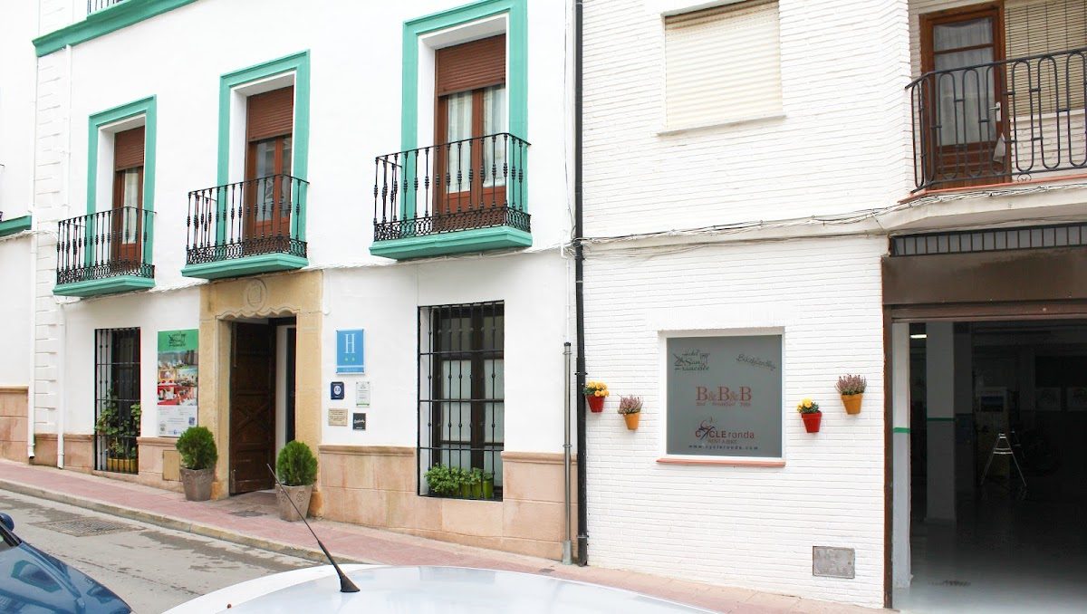 Vista exterior del Hotel San Francisco en Ronda, con paredes blancas, detalles en verde y balcones.
