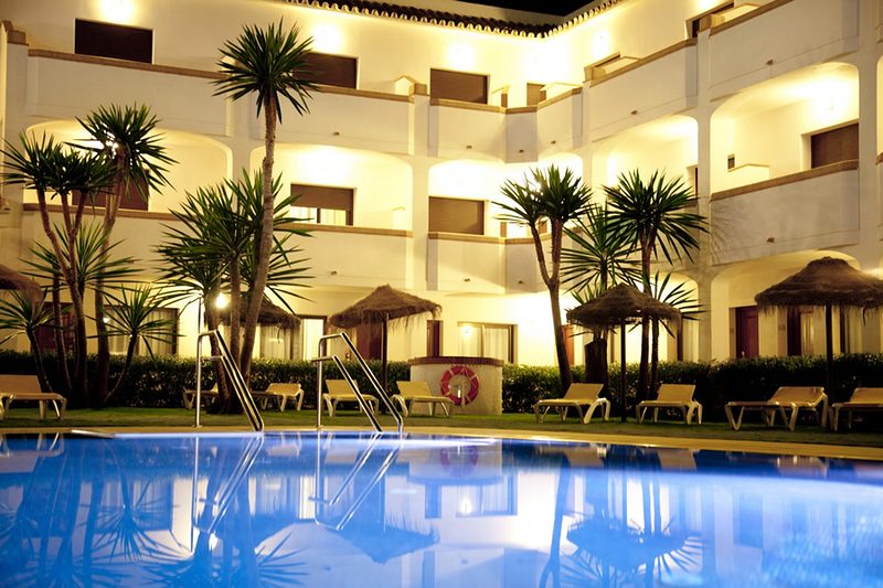 Hotel Tarik features a swimming pool surrounded by palm trees and lounge chairs in a well-lit courtyard.