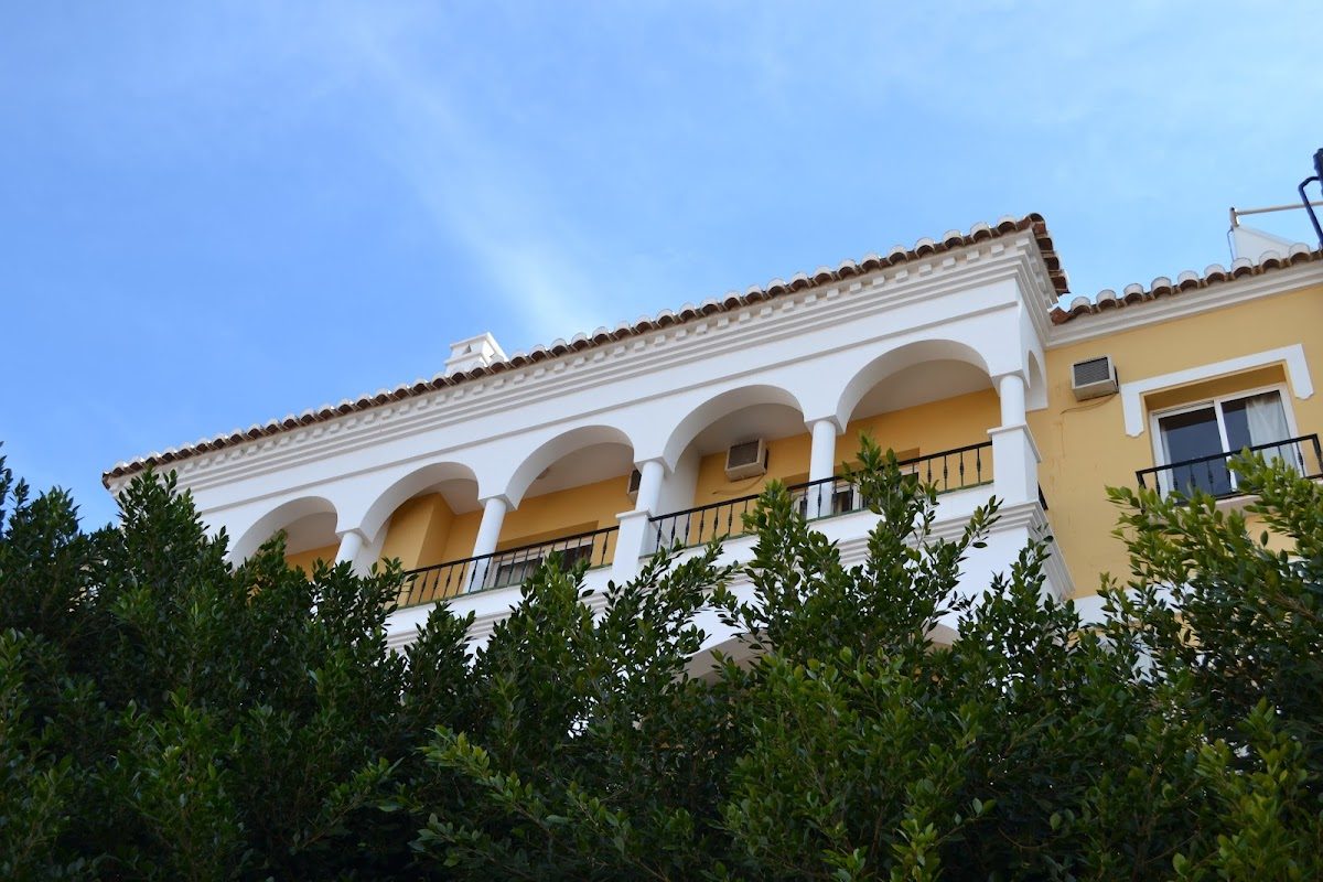 Hotel Toboso Chaparil features a yellow and white façade with arched balconies surrounded by greenery.