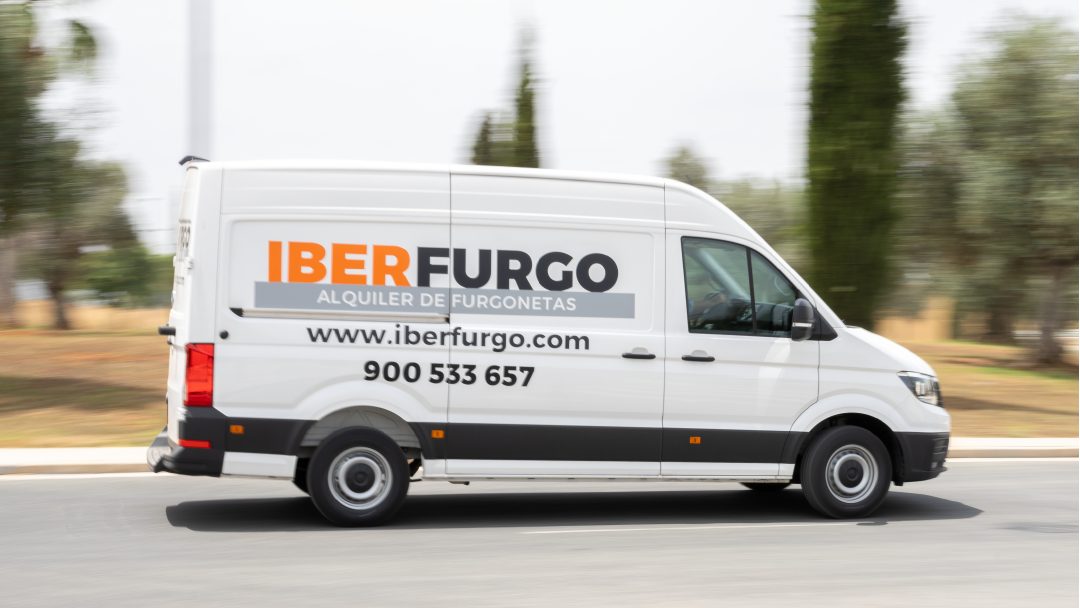 A white van with "IBERFURGO" signage drives on a road surrounded by trees.