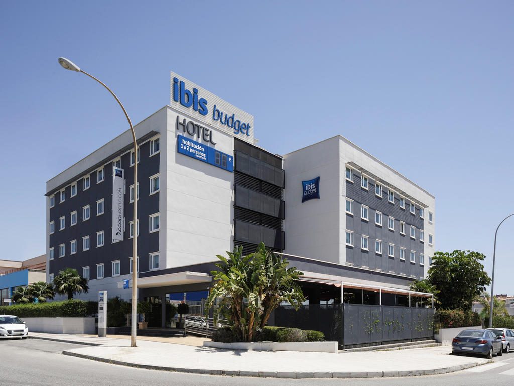El ibis budget Malaga Aeropuerto presenta un exterior moderno con una combinación de colores azul y gris y palmeras.
