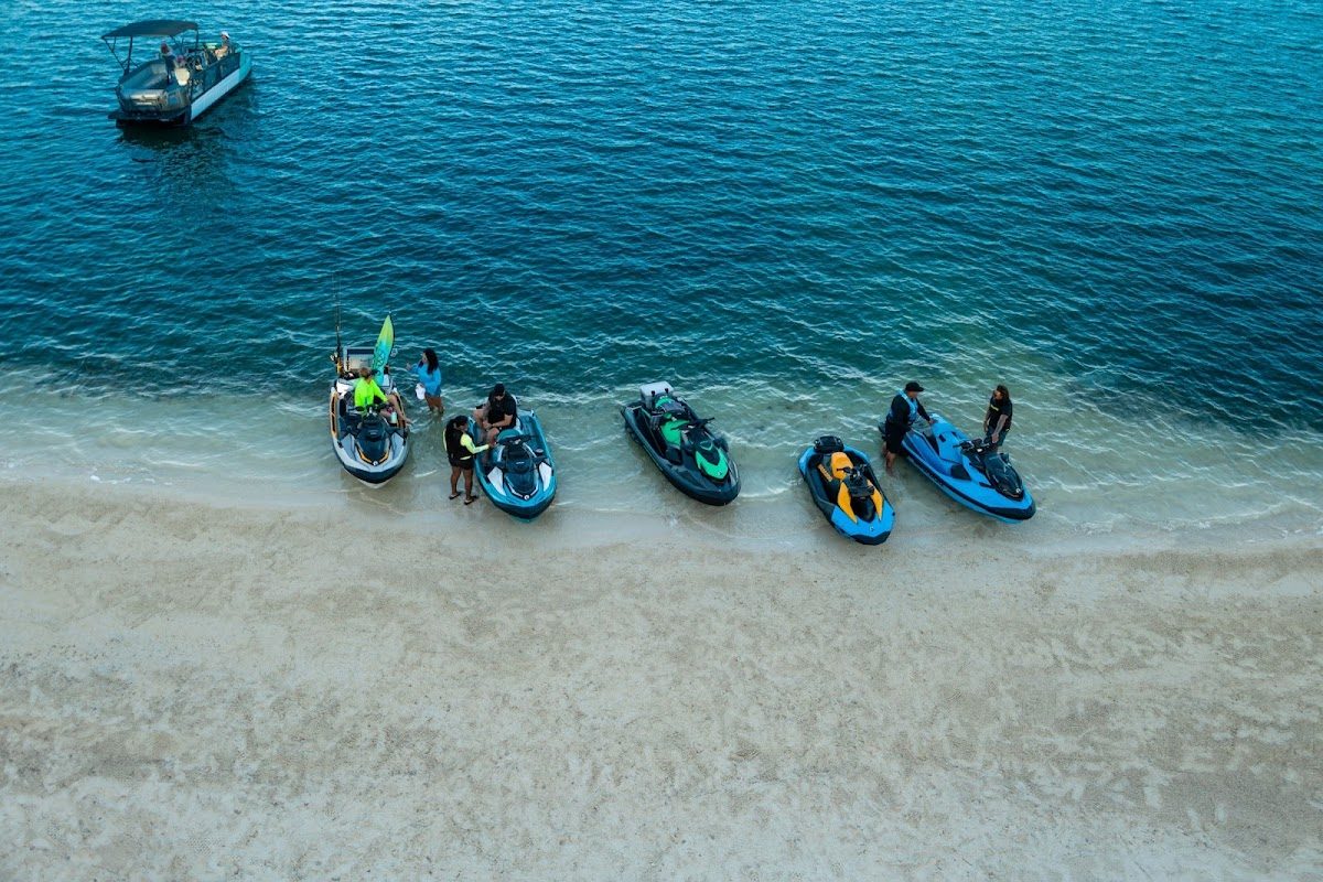 En Jet Ski Point Puerto Deportivo se pueden ver varias motos acuáticas en la playa de arena, con gente preparándose para practicar actividades acuáticas.