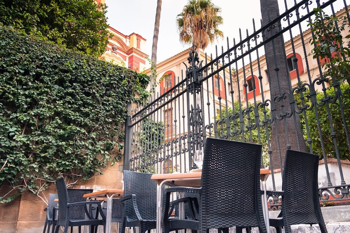 Zona de estar al aire libre con sillas de mimbre negras y mesas de madera en el restaurante Julia, rodeada de vegetación.