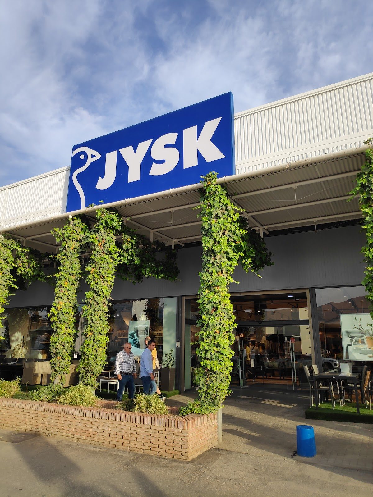 The exterior of JYSK Mijas features a blue sign and greenery around the entrance.