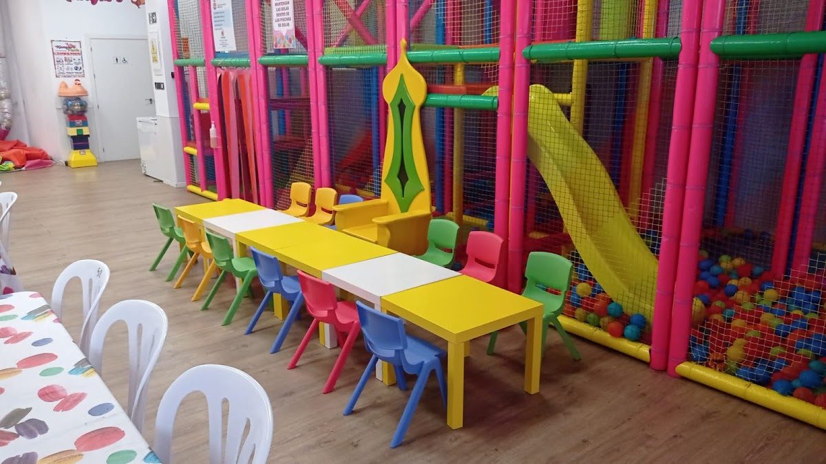 Zona de juegos de colores vivos con tobogán, piscina de bolas y mesas y sillas infantiles en el parque Kanguro.