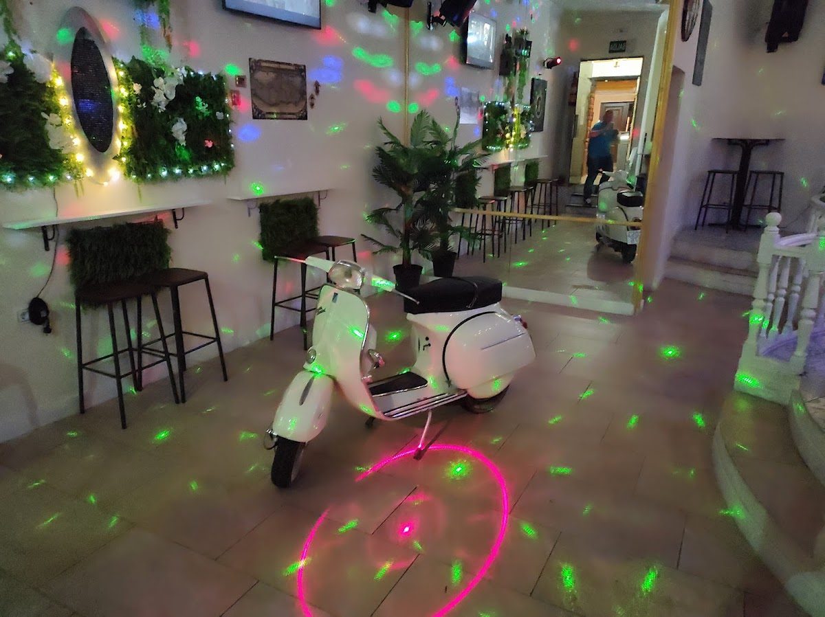 Kolon copas Latino features a white scooter and colorful lights reflecting on the walls in a lively interior.