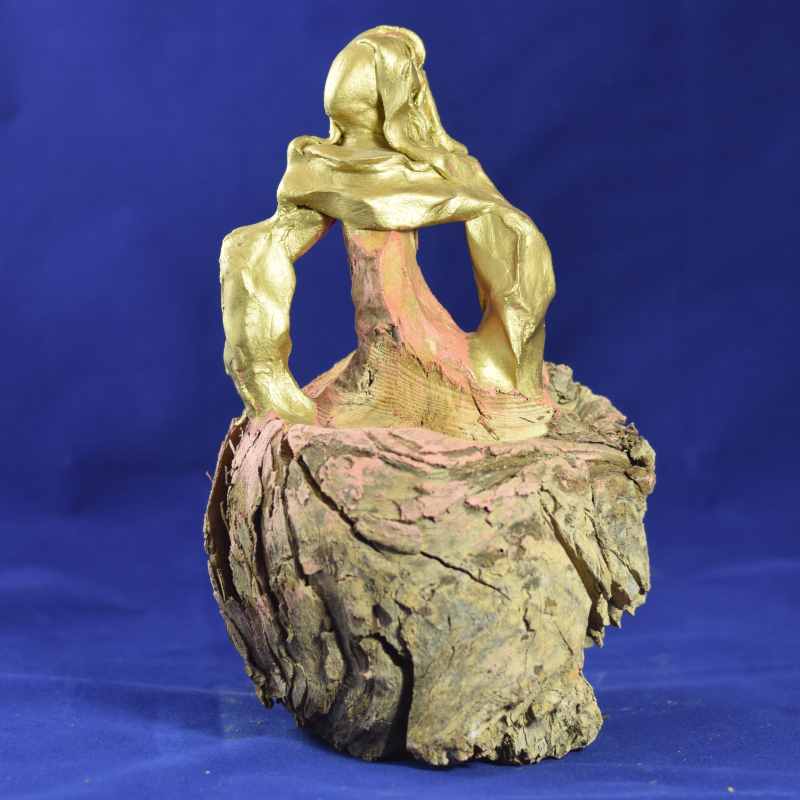 A unique sculpture featuring a gold figure seated on a textured wooden base against a blue background.