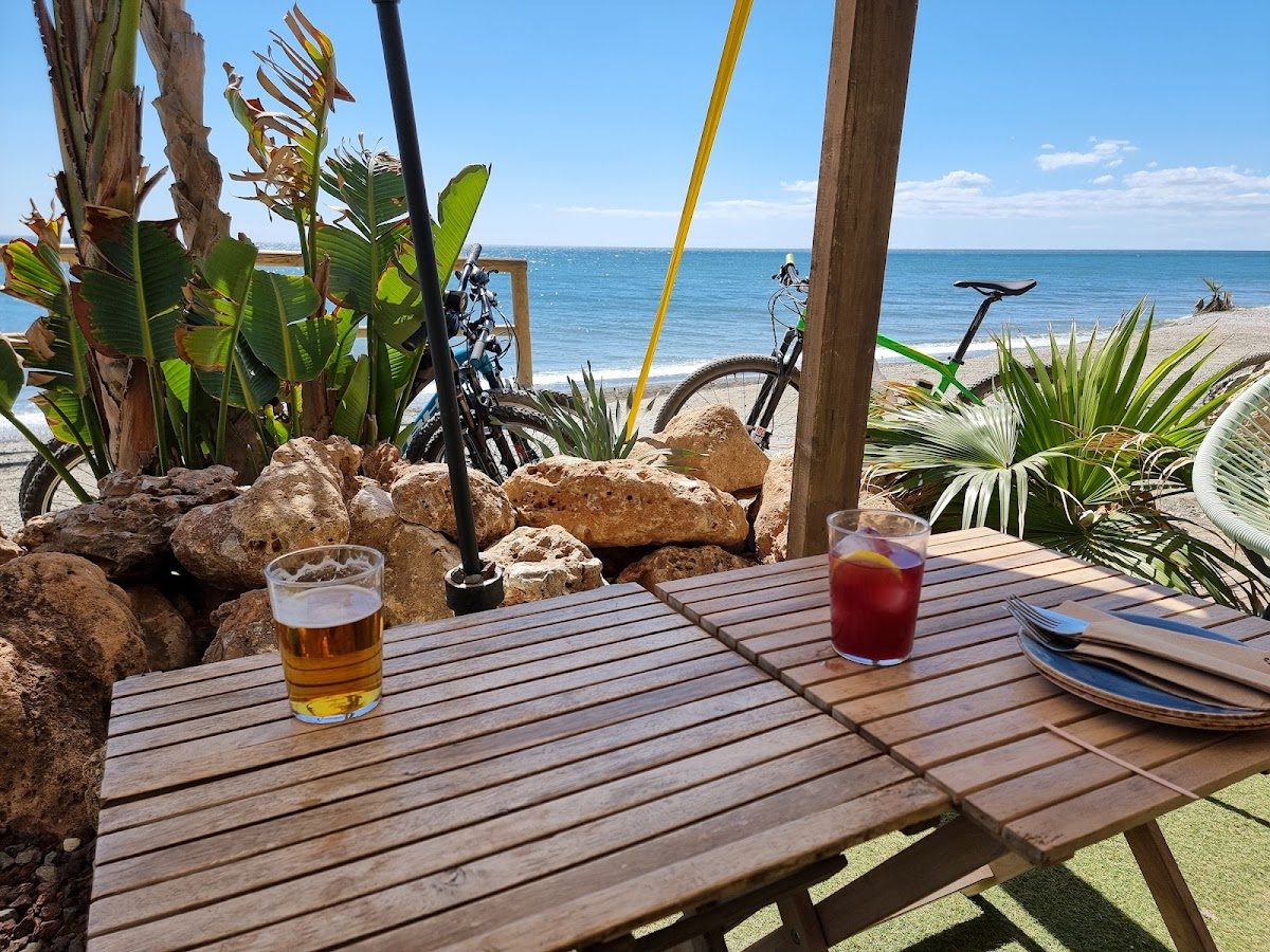 Una mesa junto al mar en La Calma Playa con bebidas, rodeada de vegetación y con vistas a la playa.
