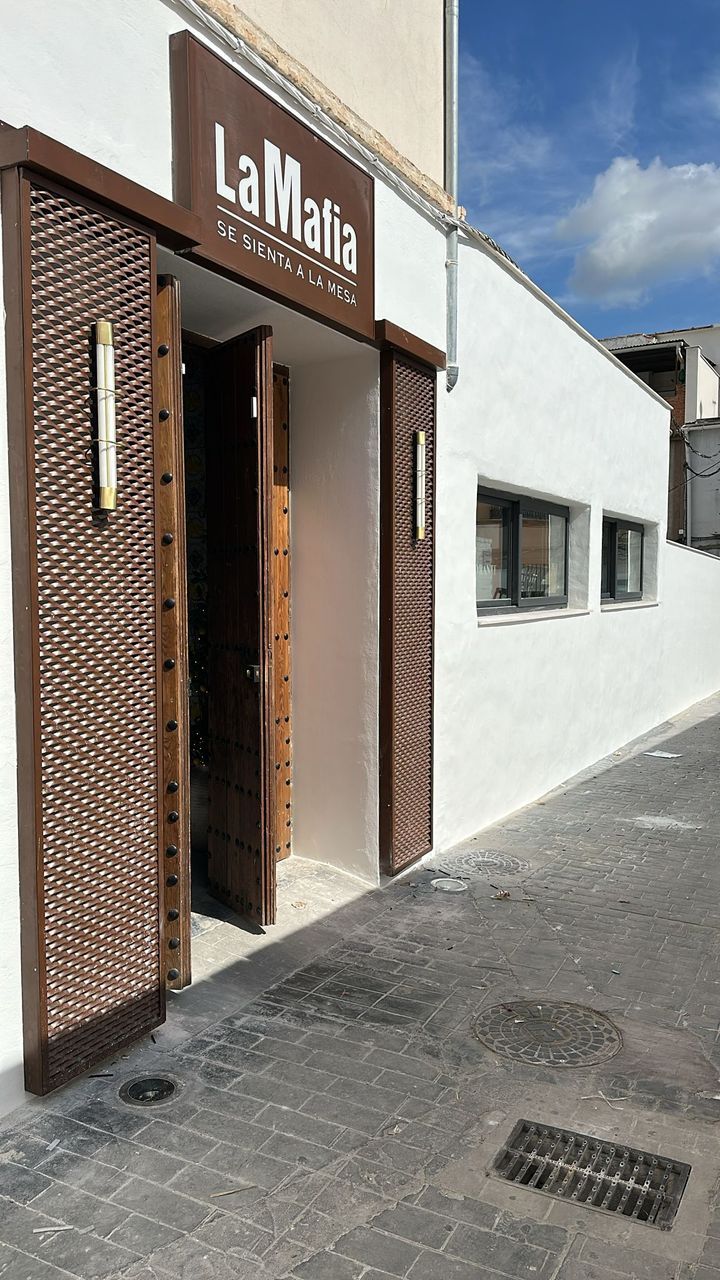 Exterior view of La Famiglia se sienta a la mesa, featuring a wooden entrance and white walls.