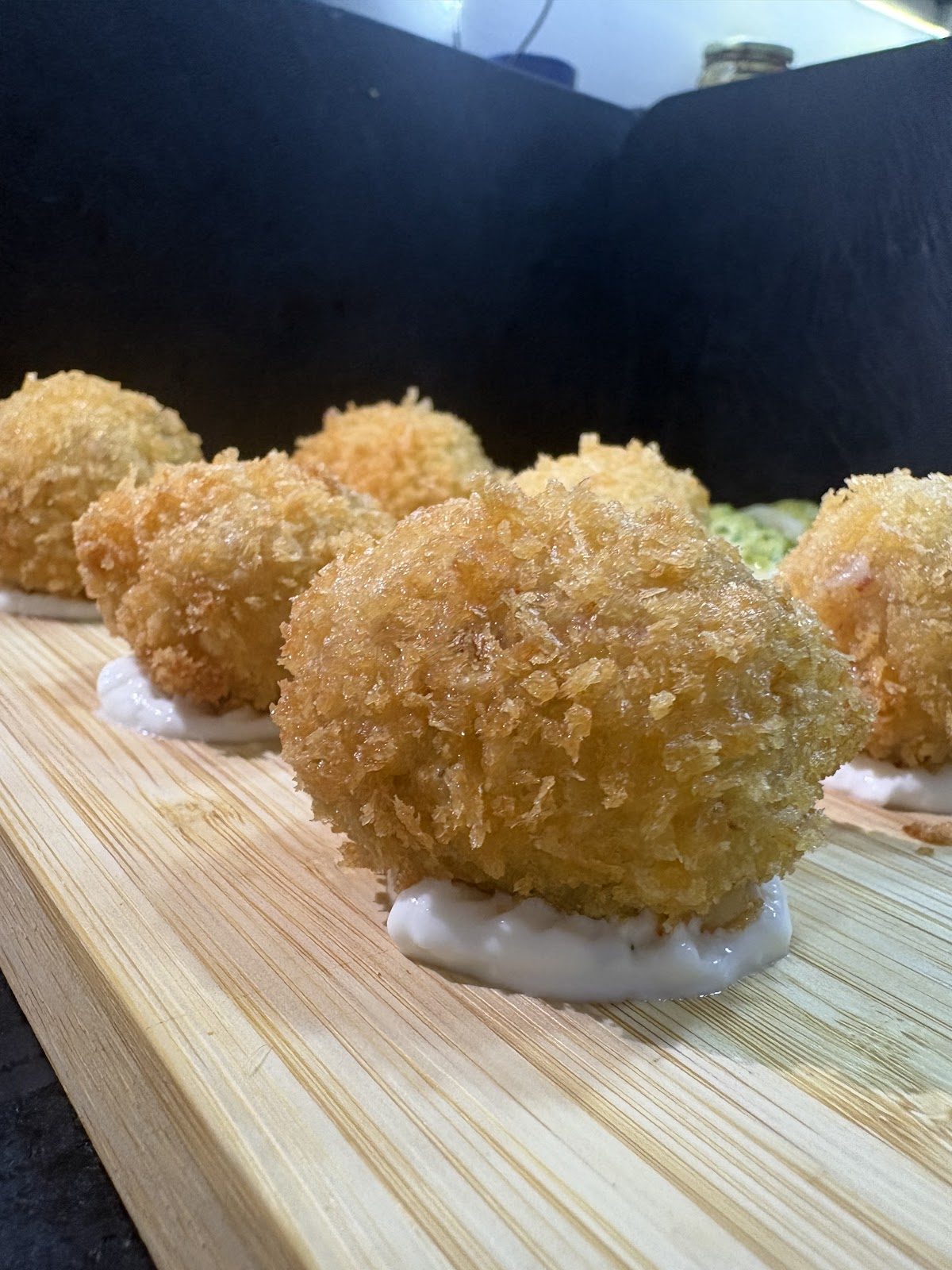 En La Trinchera Tapas, sirven crujientes bolitas de tapas fritas sobre una tabla de madera con salsa cremosa.