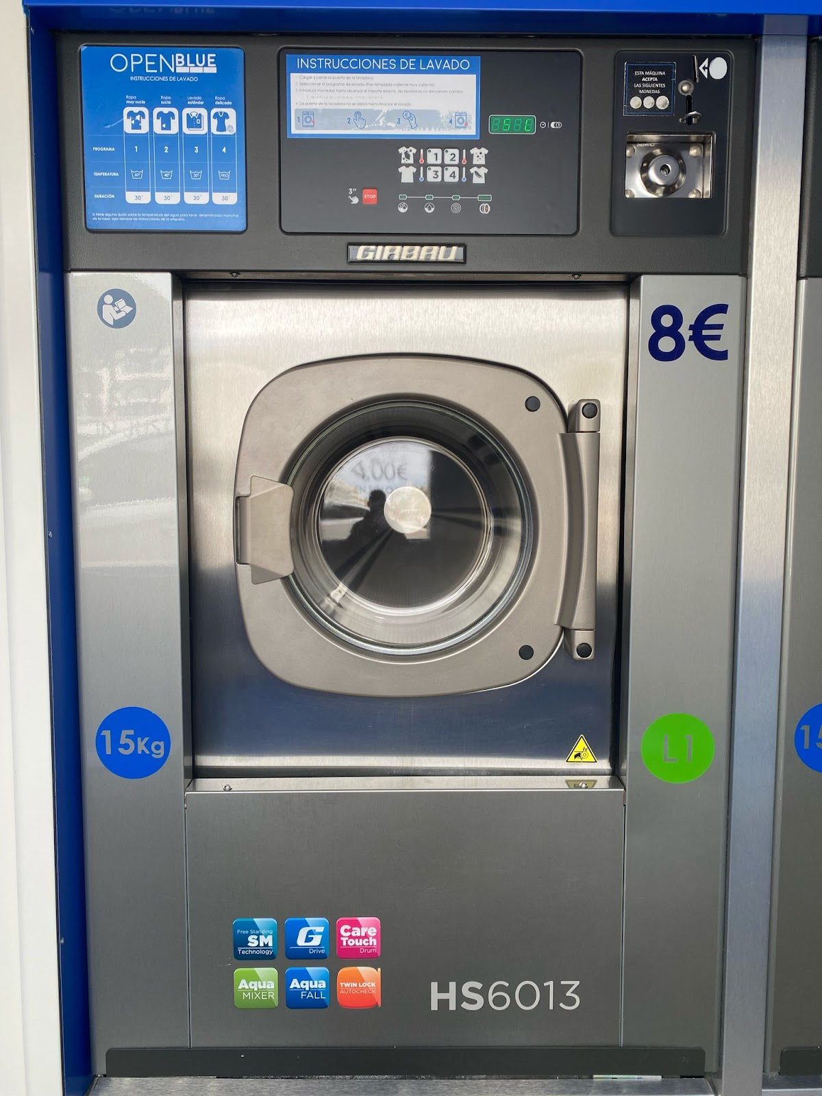 Self-service washing machine at Lavanderia Auto Servicio Open Blue, featuring a digital display and stainless steel door.