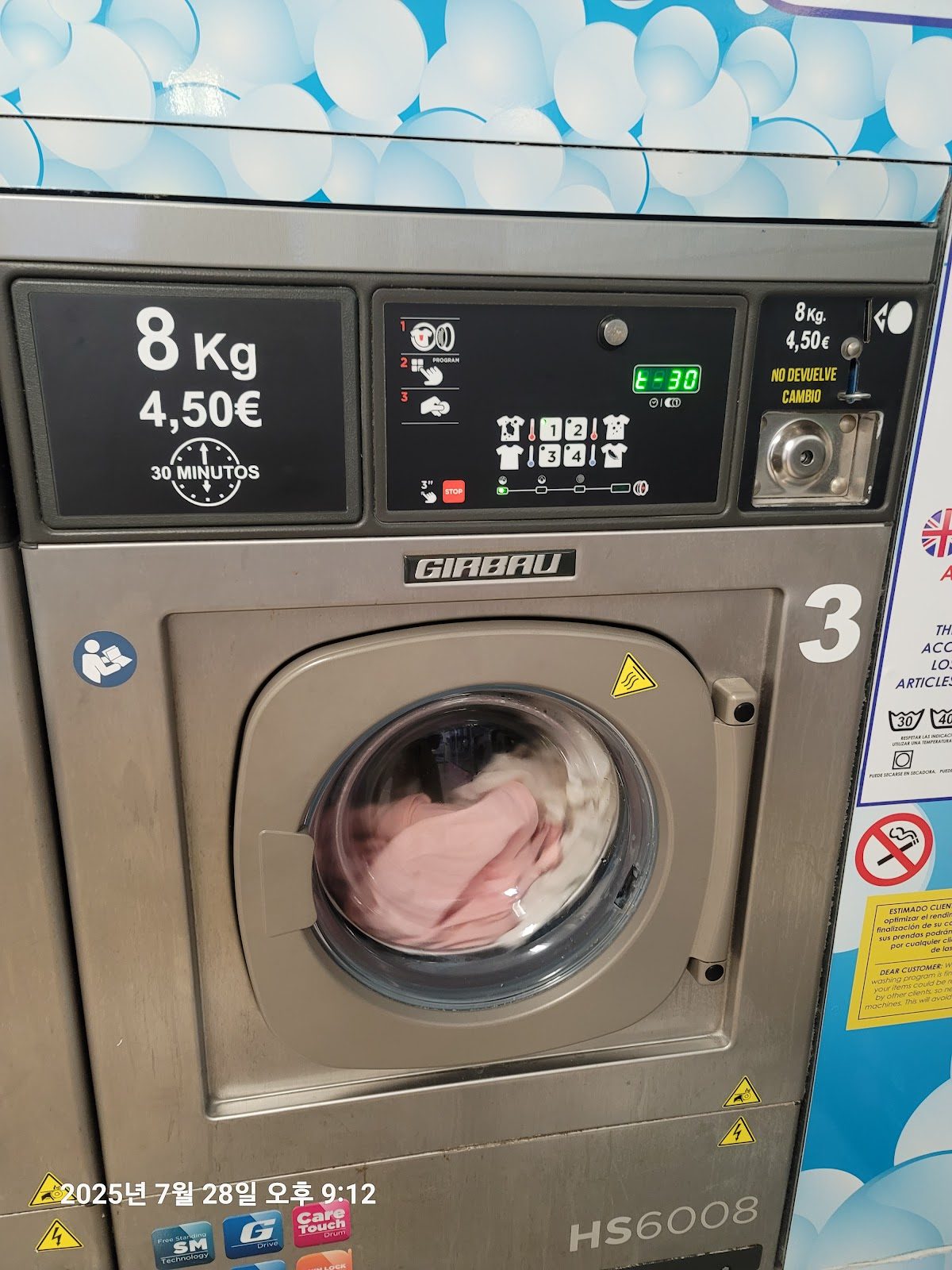 Self-service washing machine at Lavanderia autoservicio Axarquia, featuring digital controls and a clear display.
