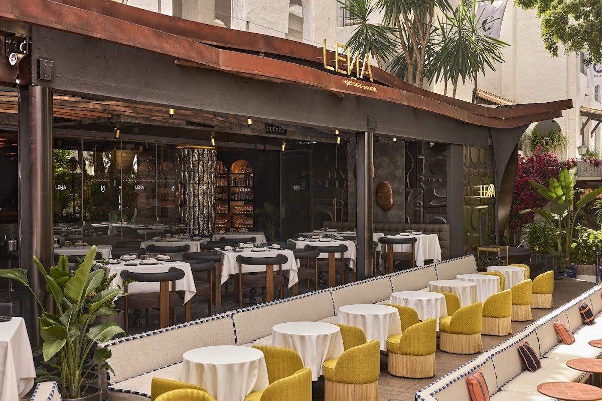 Terraza exterior con elegantes sillas amarillas y mesas blancas en el restaurante LEÑA del Hotel Puente Romano.