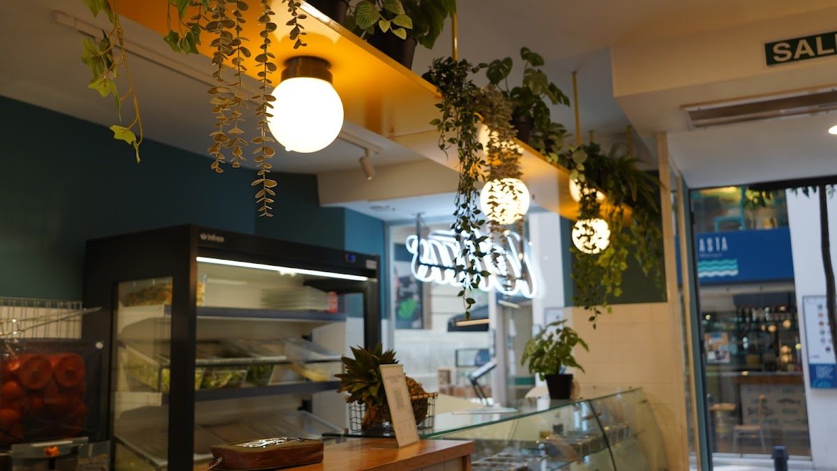 Interior de Lettus Larios con plantas, lámparas colgantes y una vitrina con opciones de alimentos saludables.