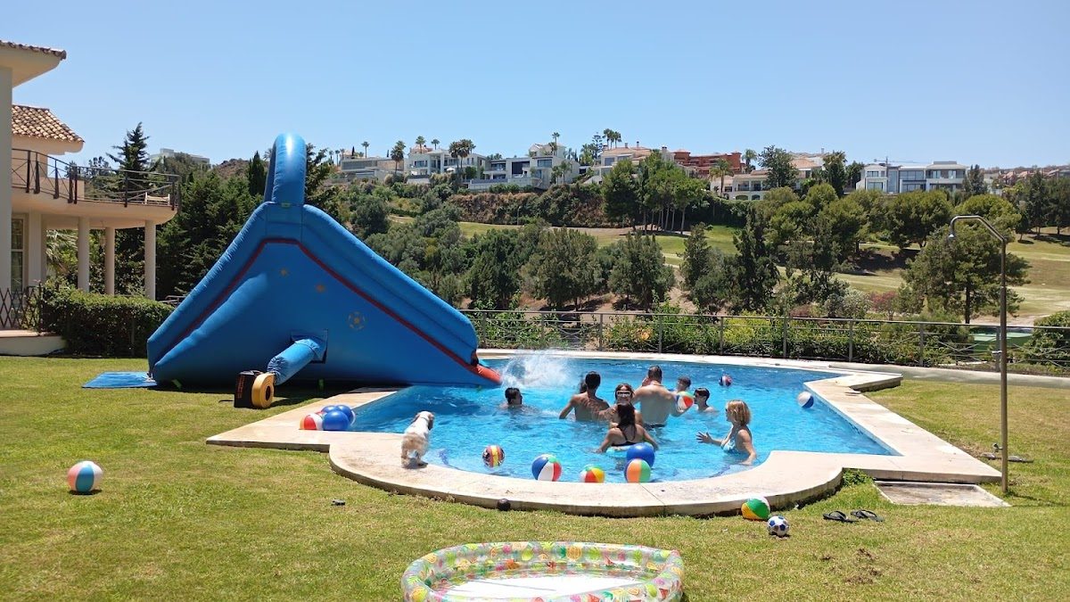Niños jugando en una piscina con tobogán, rodeados de coloridas pelotas de playa en Little Kangu.