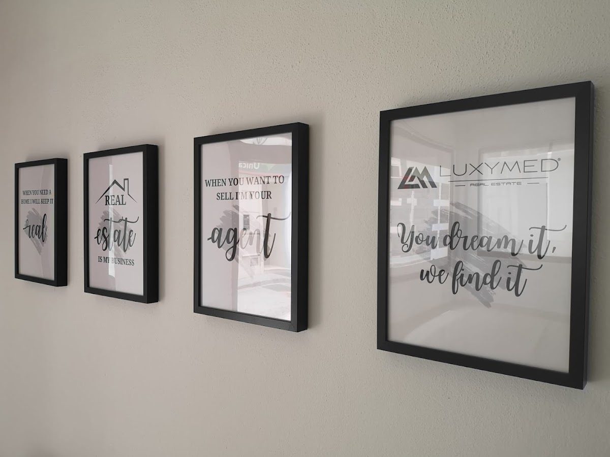 Frases motivacionales enmarcadas y el logotipo de Luxymed Real Estate expuestos en una pared.