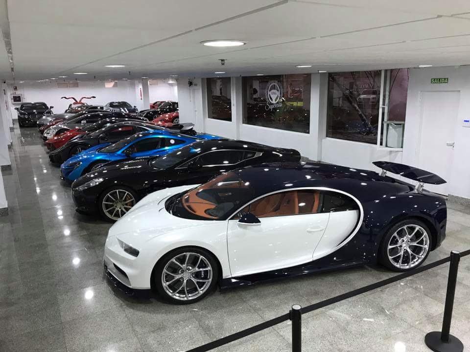 Una sala de exposición que muestra una variedad de superdeportivos de lujo, incluyendo un Bugatti blanco y azul.