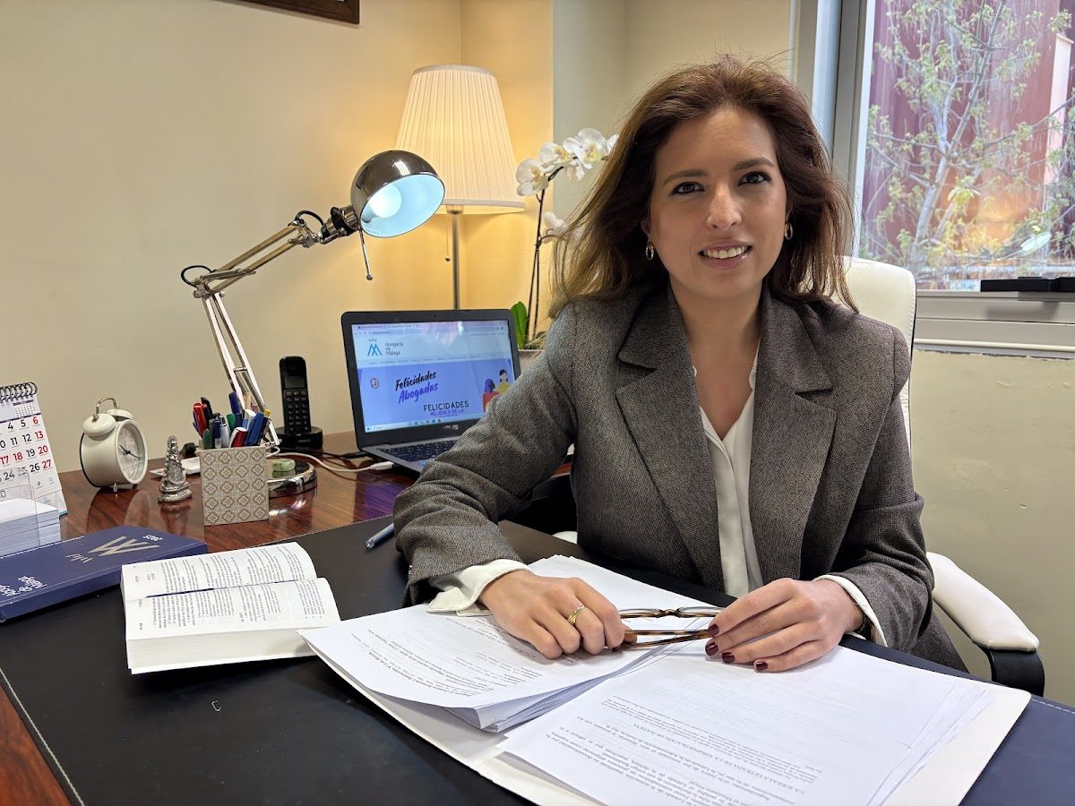 A lawyer sits at a desk with documents, a lamp, and a computer displaying a professional website.