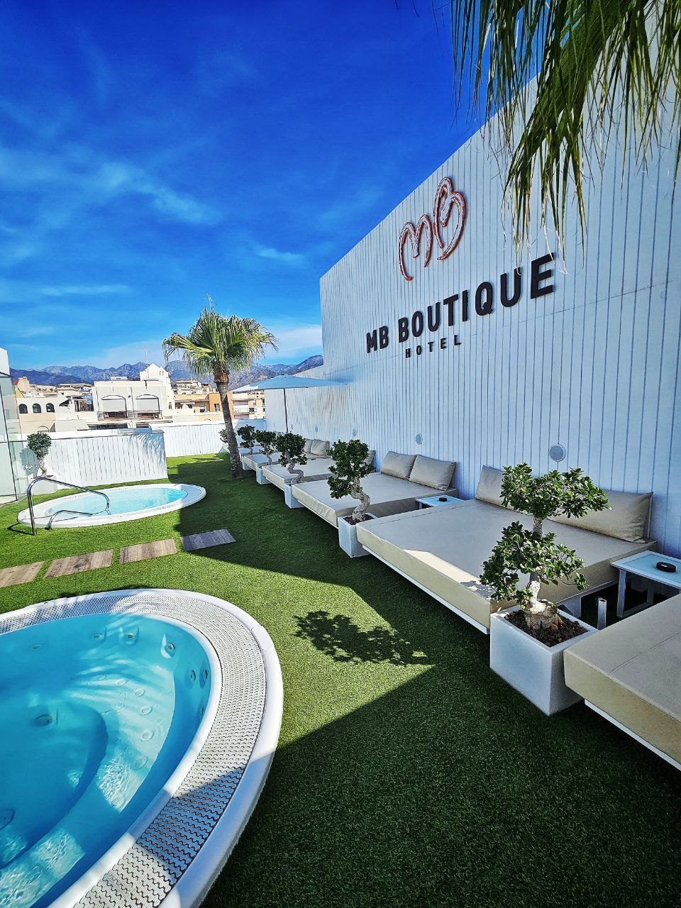 The MB Boutique Hotel features a pool area with loungers and a hot tub surrounded by greenery.