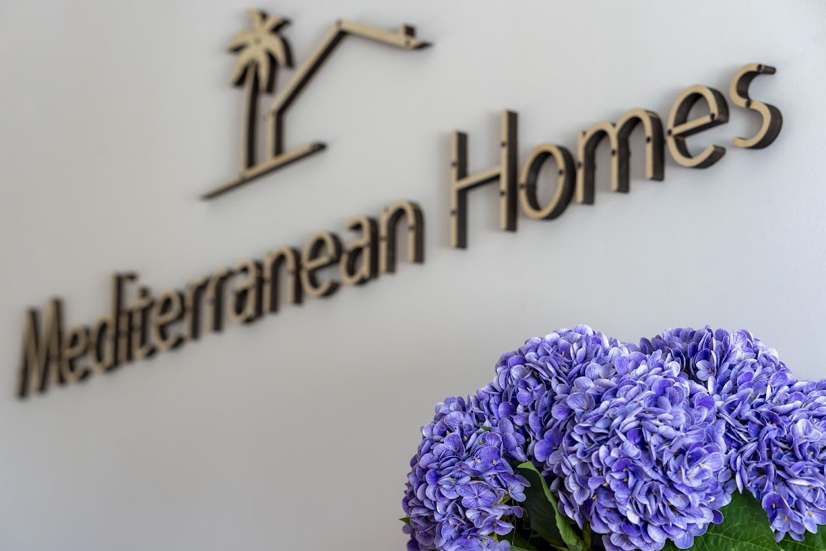 El letrero de Mediterranean Homes está expuesto en una pared, acompañado de un ramo de hortensias moradas.