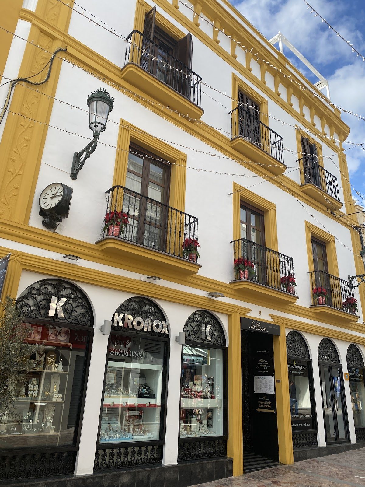 El exterior del Mercadillo de Nerja presenta un edificio blanco con detalles amarillos y balcones decorativos.