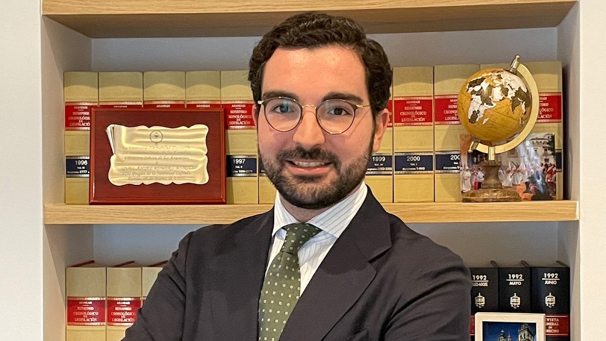 Miguel Ángel Romero Murillo stands confidently in front of a bookshelf filled with legal books and awards.