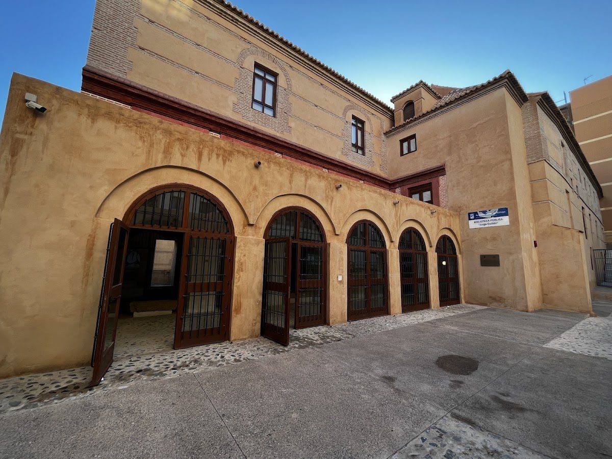 The Municipal Public Library Jorge Guillen features a historic building with arched doorways and a textured exterior.