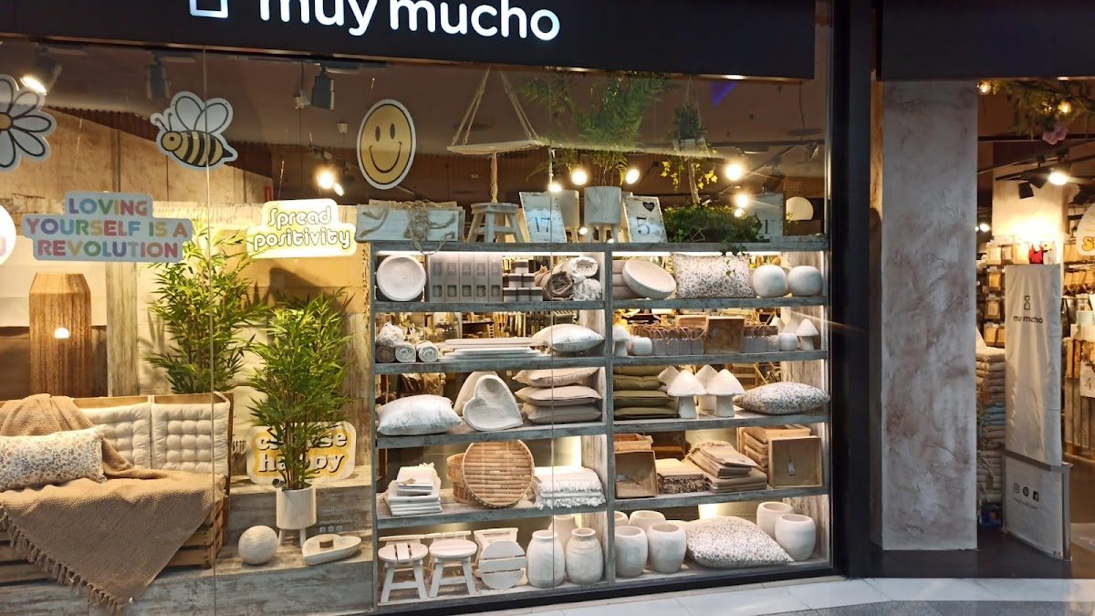 El escaparate de Muy Mucho Torremolinos exhibe una variedad de artículos de decoración para el hogar y textiles.
