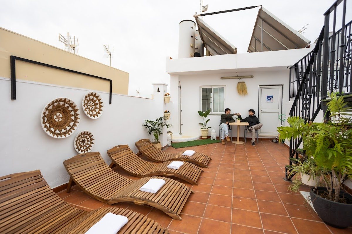 Naim Guest House Nerja features a terrace with wooden loungers and guests relaxing at a table.