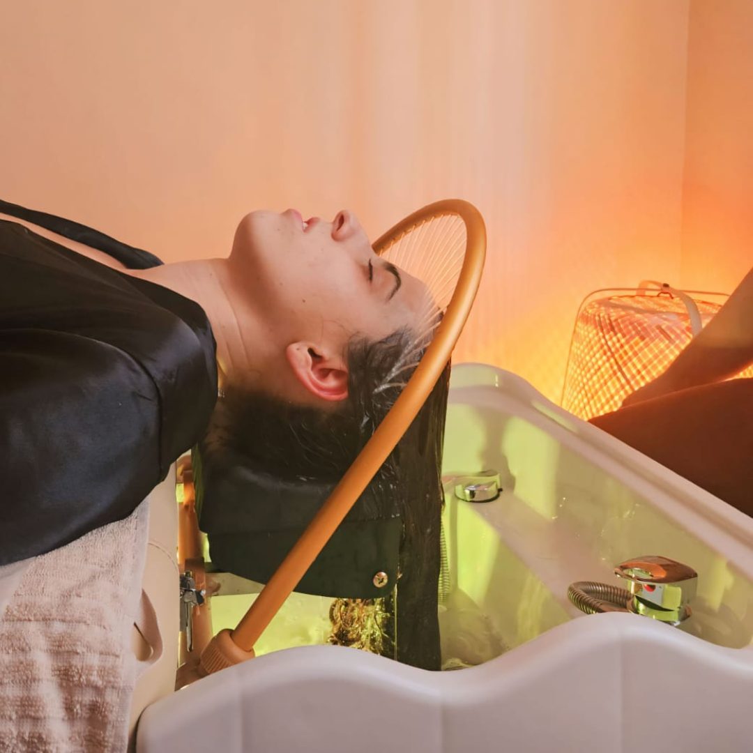 Una clienta se relaja durante un tratamiento capilar en Neha Estética y Bienestar, rodeada de una iluminación relajante.