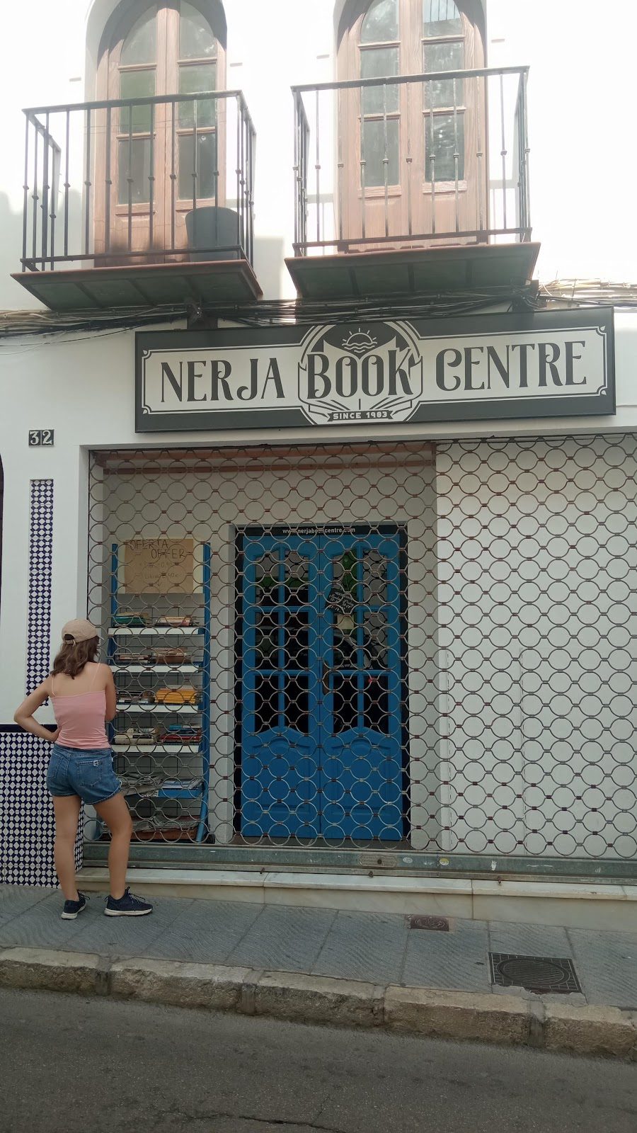 A person stands outside the closed Nerja Book Centre, featuring a blue door and decorative signage.