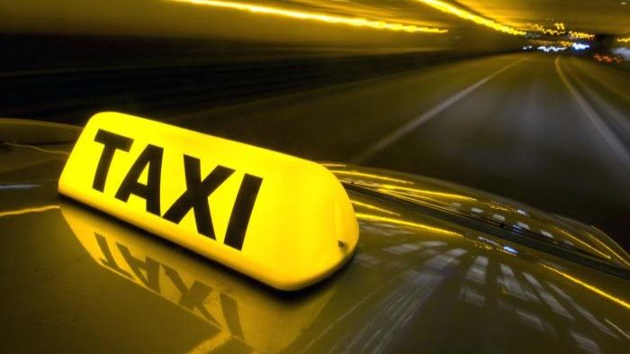 A taxi sign illuminated in yellow on the roof of a moving vehicle.