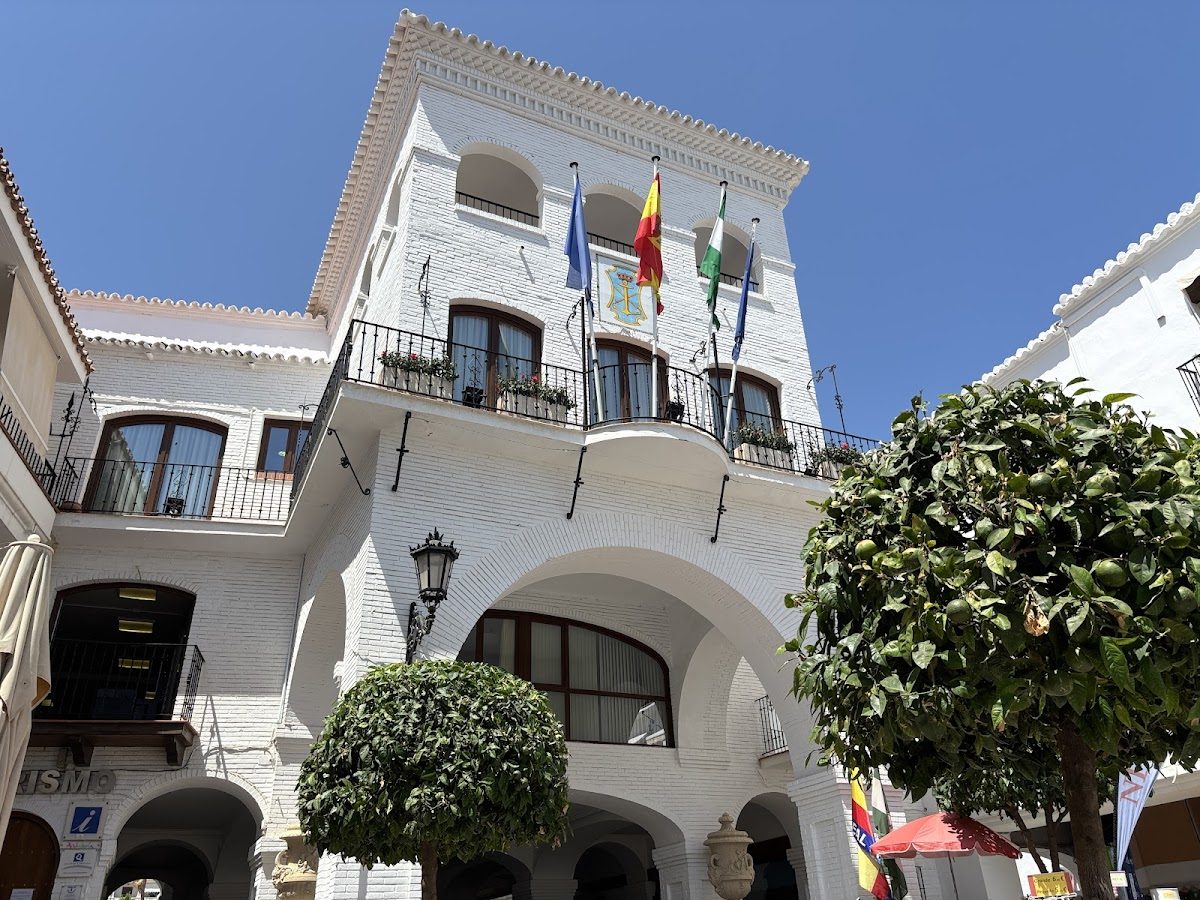 The Nerja Town Hall features a white facade with flags and decorative balconies under a clear blue sky.