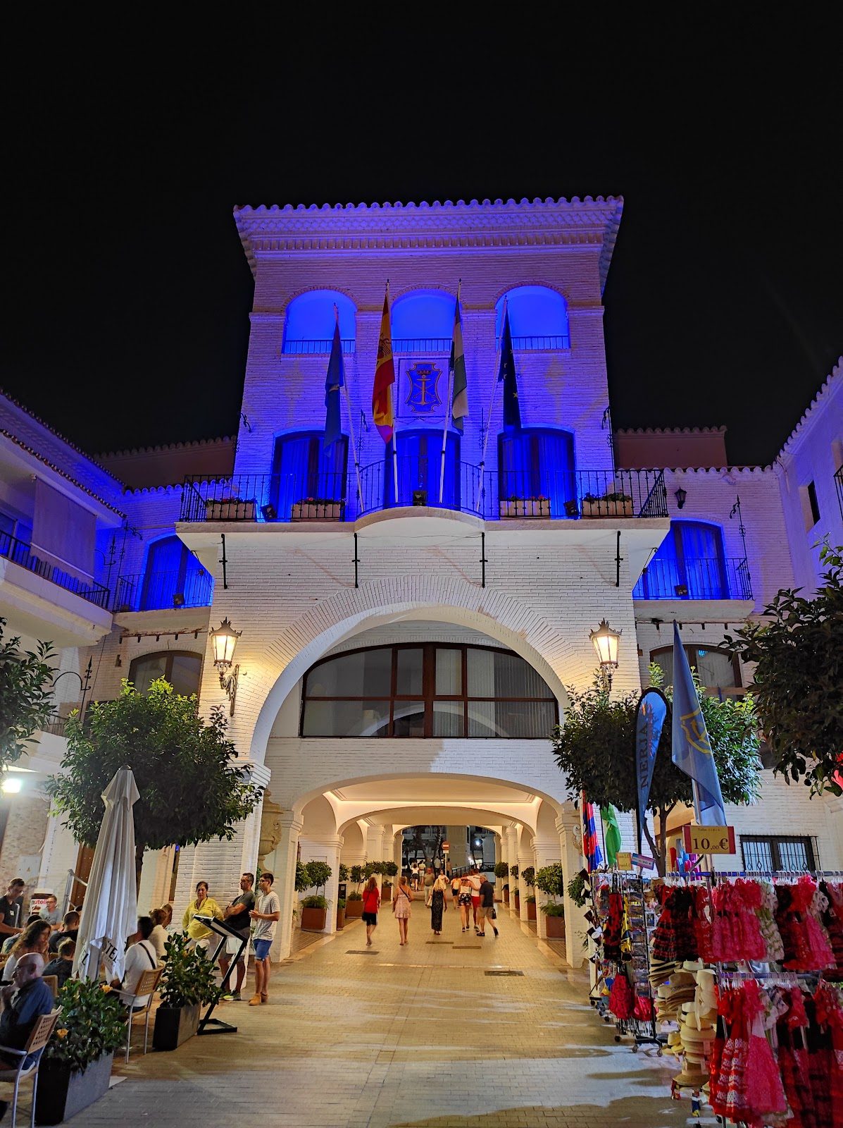NerjaRooms features a beautifully lit exterior with flags and vibrant blue lighting at night.