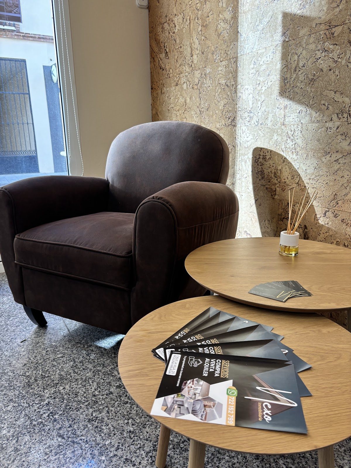 A cozy seating area with a brown armchair and promotional brochures on a wooden table at Nexo Inmobiliaria.