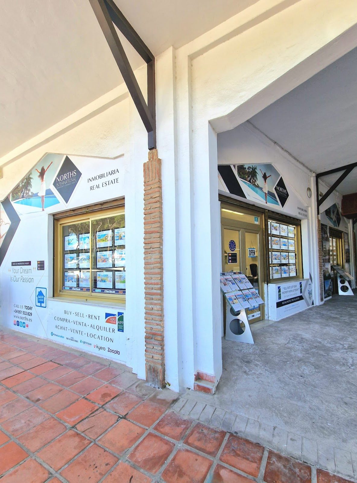Local comercial de Norths International Property con grandes ventanales que exhiben listados de propiedades inmobiliarias en C.C. El Campanario, Calahonda.