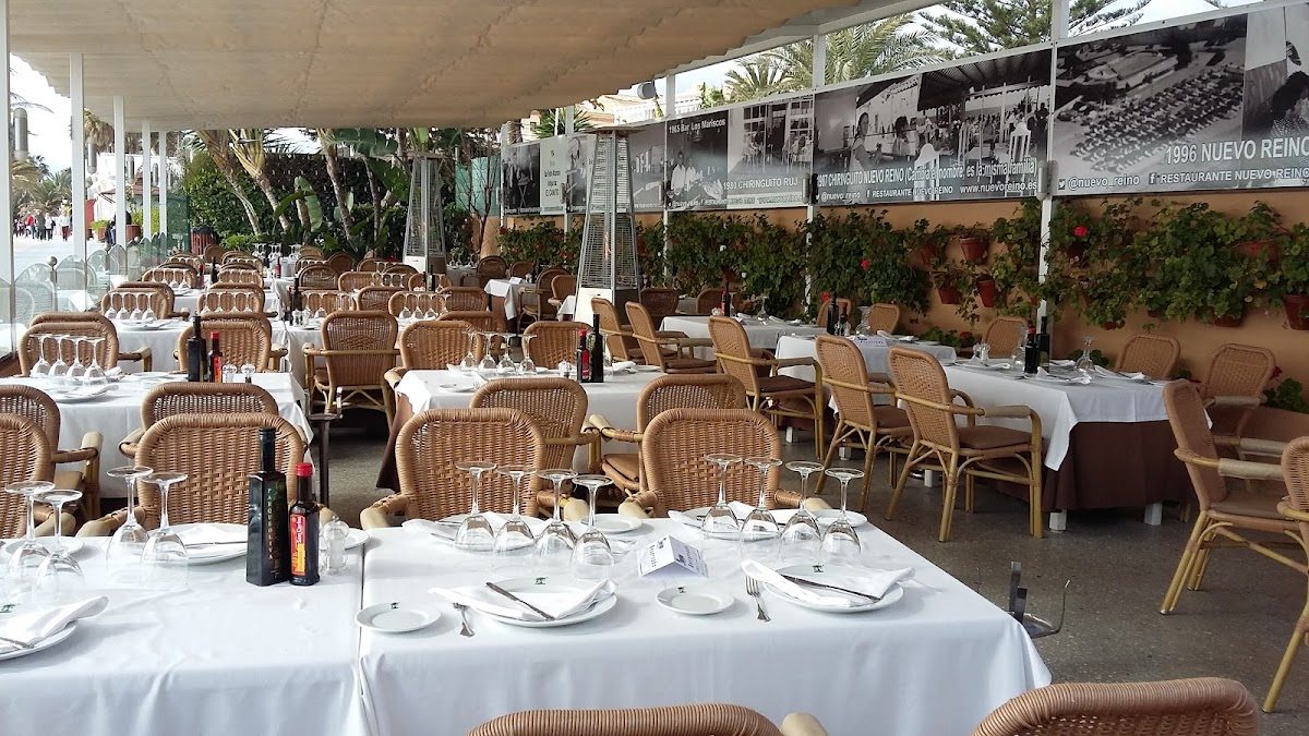 Comedor al aire libre en Nuevo Reino con mesas cuidadosamente dispuestas y un telón de fondo de vegetación y fotos históricas.