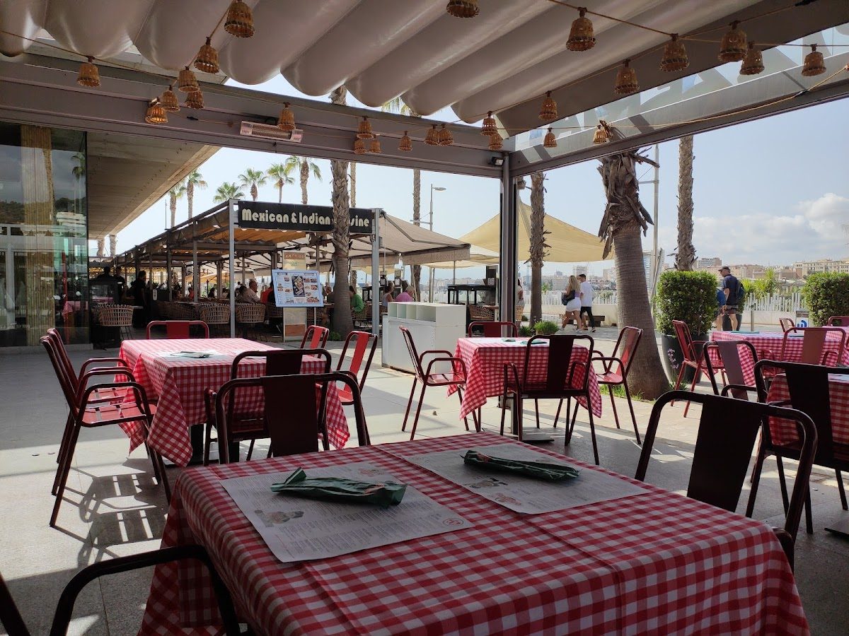 Outdoor seating area with checkered tablecloths at O Mamma Mia in Muelle Uno, Málaga, overlooking the waterfront.