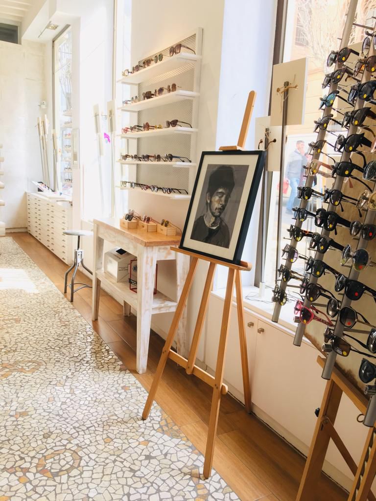 Interior of Óptica VISUAL Málaga featuring sunglasses displays, a wooden easel with artwork, and a mosaic floor.