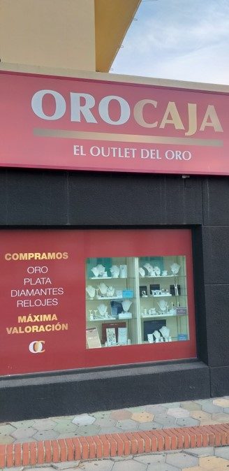 The storefront of Oro Caja features a display of jewellery and a prominent sign indicating it is an outlet for gold.
