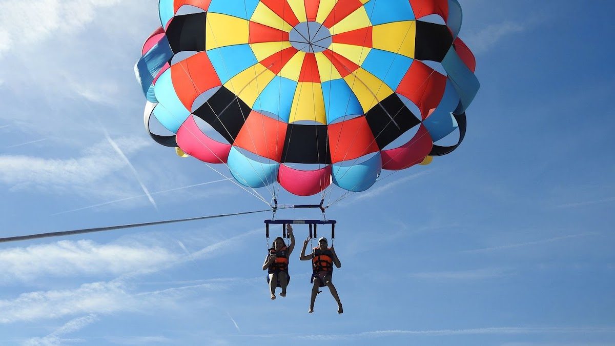 Two people parasailing under a colorful parachute against a clear blue sky.