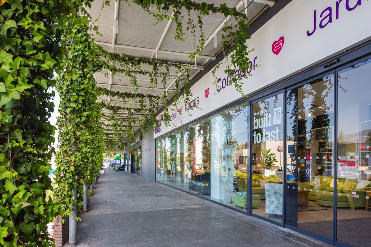 El exterior del Parque Comercial Miramar presenta un diseño moderno con vegetación a lo largo del paseo y grandes escaparates de cristal.