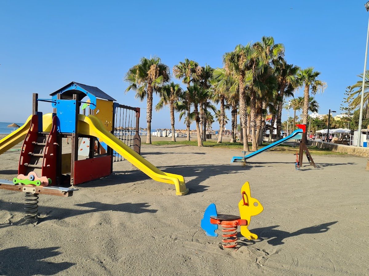 Juegos infantiles coloridos con toboganes y balancines rodeados de palmeras cerca de la playa.
