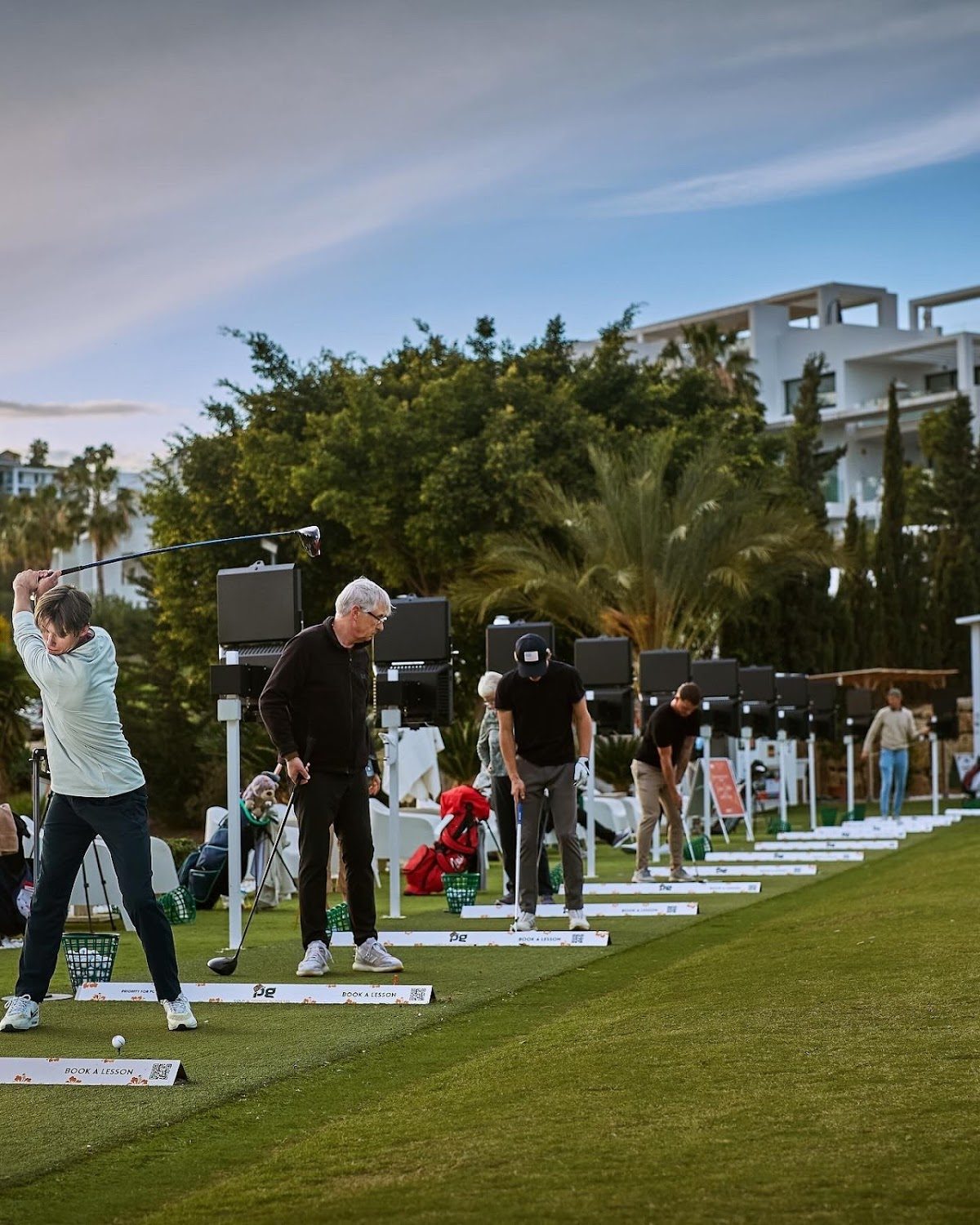 PG Golf & Sports Academy features golfers practicing at the Trackman Range with lush greenery in the background.