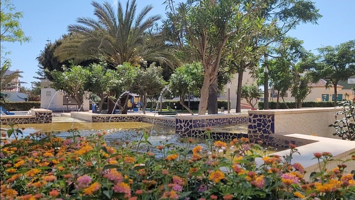 Plaza María Zambrano features vibrant flowers, palm trees, and a serene water fountain in a sunny park setting.