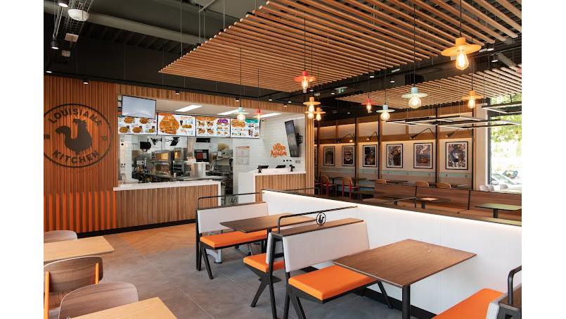El restaurante Popeyes Famous Louisiana Chicken cuenta con un interior moderno con detalles de madera e iluminación colorida.